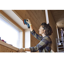 Frau schleift Holz mit einem Exzenterschleifer in einem hellen Raum.