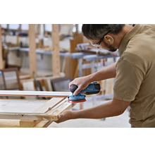 Ein Mann schleift mit einem Exzenterschleifer ein Holzstück in einer Werkstatt.