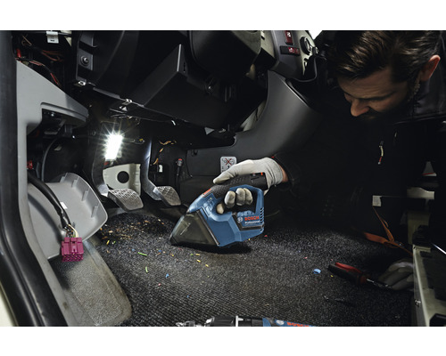 Ein Mann saugt mit einem Akkusauger den Fußraum eines Fahrzeugs.