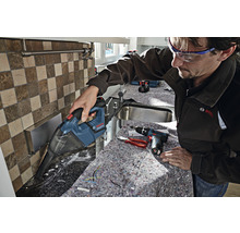 Ein Mann saugt mit einem Akku-Handsauger Späne von einer Küchenarbeitsplatte. Werkzeuge liegen bereit.