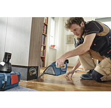 Handwerker arbeitet mit einem Bohrhammer auf einem Holzboden neben einem Regal und einem Werkzeugkoffer. Bosch Logo.