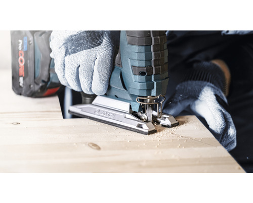 Person schneidet Holz mit einer Stichsäge, wobei sie Handschuhe trägt