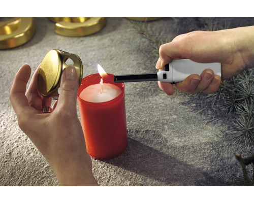 Eine Person zündet mit einem Stabfeuerzeug eine Kerze an. Der Kerzendeckel wird in der Hand gehalten.