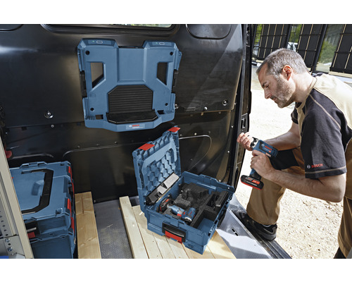 Ein Handwerker im Laderaum eines Transporters mit Werkzeugkoffer, montiertes Regalsystem und Akkugerät in der Hand.