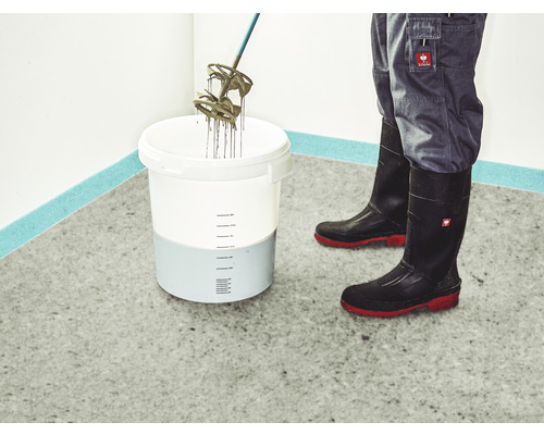 Mörtel wird in einem Eimer mit einem Rührwerk gemischt, getragen werden Gummistiefel und eine Arbeitshose.