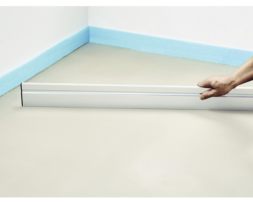 Person nivelliert Estrich mit Richtscheit und Dämmstreifen an der Wand