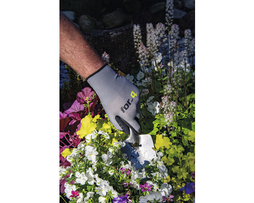 Person mit Gartenhandschuhen und Pflanzschaufel beim Pflanzen von Blumen