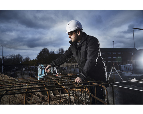 Ein Bauarbeiter mit Schutzhelm verwendet einen Akku-Bindeautomat auf einer Baustelle.