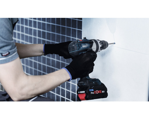 Eine Person bohrt mit einer Bohrmaschine ein Loch in eine Fliesenwand.