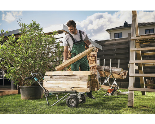 Mann belädt Transportwagen mit Brennholz im Garten.