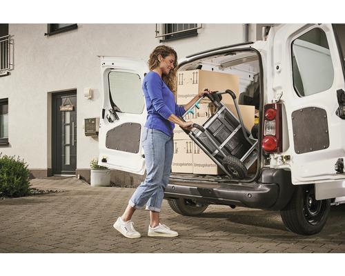 Frau lädt mit einer Sackkarre Umzugskartons in einen Transporter.