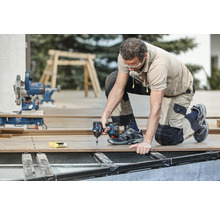 Ein Handwerker kniet auf einer Terrasse und arbeitet mit einem Akku-Schlagschrauber.
