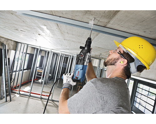Ein Arbeiter bohrt mit einer Schlagbohrmaschine ein Loch in die Decke eines Rohbaus.