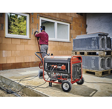 Ein Stromgenerator versorgt eine Baustelle mit Energie, während ein Bauarbeiter an einer Wand arbeitet.