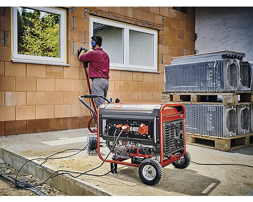 Ein Stromgenerator versorgt eine Baustelle mit Energie, während ein Bauarbeiter an einer Wand arbeitet.