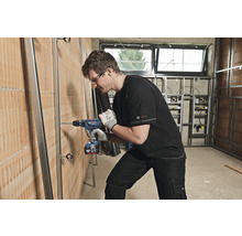 Handwerker bohrt mit einem Akku-Bohrschrauber ein Loch in eine Wand, auf der Metallprofile angebracht sind.