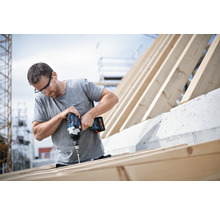 Ein Handwerker befestigt mit einem Akku-Bohrschrauber Schrauben an einem Holzrahmen.