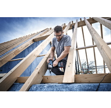 Handwerker arbeitet mit einem Akku-Schlagschrauber an einem Dachstuhl aus Holz.