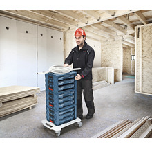 Handwerker schiebt einen Werkzeugwagen mit mehreren Schubladen in einem Rohbau.