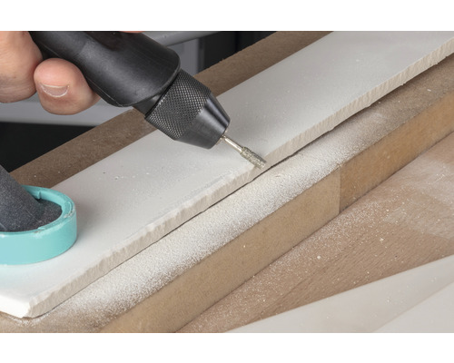 Eine Person verwendet ein Multifunktionswerkzeug, um eine weiße Fliese zu bearbeiten.