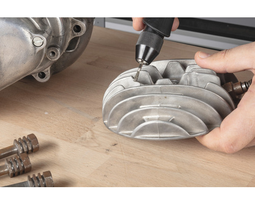 Eine Person bearbeitet einen Zylinderkopf mit einem Multifunktionswerkzeug auf einer Werkbank.