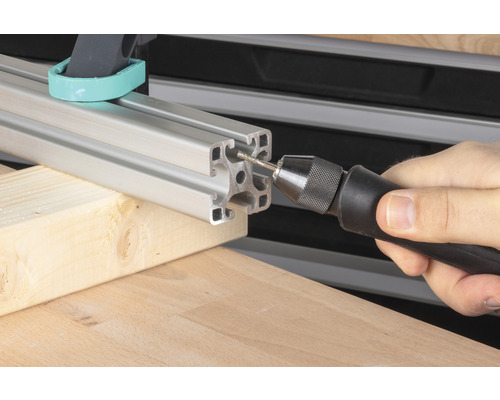 Eine Person bohrt mit einem Handbohrer ein Loch in ein Aluminiumprofil.