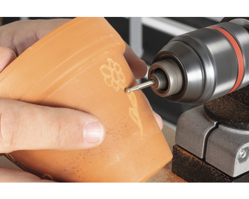 Nahaufnahme einer Person, die mit einem Dremel eine Blume in einen Blumentopf graviert.