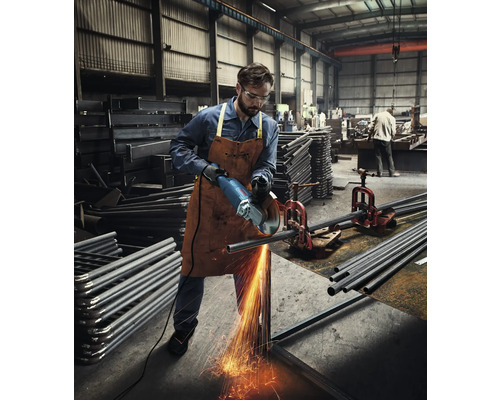 Mann schneidet Metallrohr mit einem Winkelschleifer in einer Werkstatt.