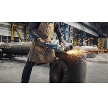 Ein Arbeiter in einer Werkshalle verwendet einen Winkelschleifer an einem Metallrohr, wobei Funken sprühen.