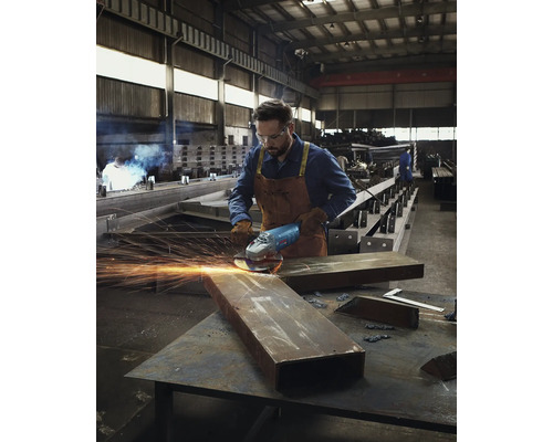 Ein Mann mit Schutzbrille und Handschuhen schleift Metall mit einem Winkelschleifer in einer Werkstatt.