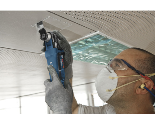 Mann schneidet Deckenplatte mit Multifunktionswerkzeug