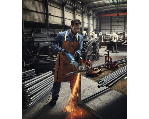 Mann schneidet Metallrohr mit Winkelschleifer in Werkstatt