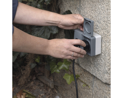 Person schließt Stecker an Außensteckdose an