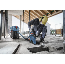 Ein Arbeiter, der eine Mauernutfräse in einem Gebäude mit einem Industriestaubsauger verwendet.