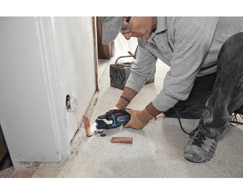 Mann schneidet mit einem Multifunktionswerkzeug ein Kupferrohr in einem Raum.