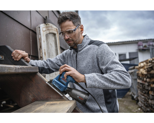 Mann schleift Holztreppe mit einem Schwingschleifer von Bosch