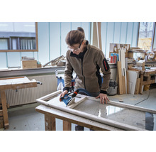 Frau schleift Holzrahmen mit Schleifgerät in Werkstatt