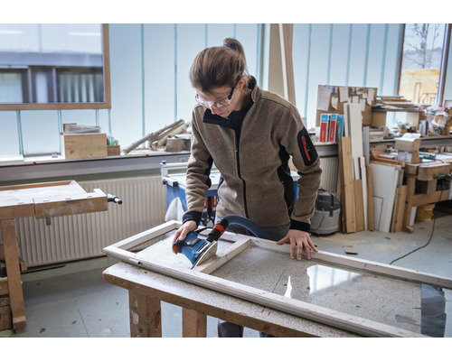 Frau schleift Holzrahmen mit Schleifgerät in Werkstatt