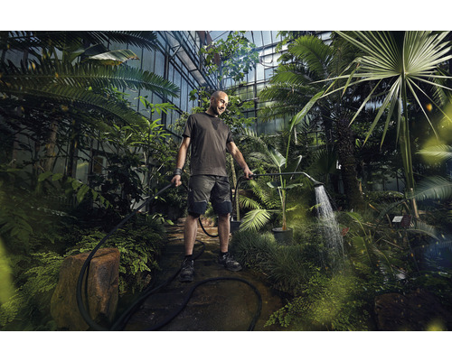 Ein Mann gießt Pflanzen in einem Gewächshaus mit einer Gartendusche.