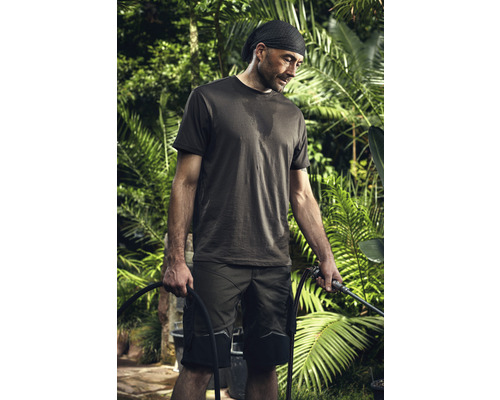 Ein Mann in Arbeitskleidung hält einen Gartenschlauch in einem Garten.