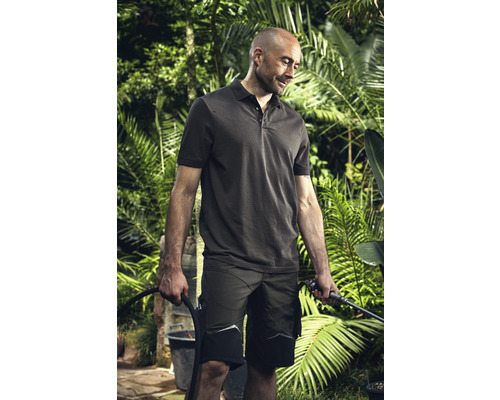 Mann mit Poloshirt und Arbeitsshorts, der im Garten Pflanzen bewässert