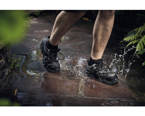 Person geht mit Sicherheitsschuhen durch eine Wasserpfütze