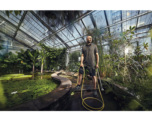 Mann mit Wasserschlauch und Teichschlammsauger in einem Gewächshaus mit Teich