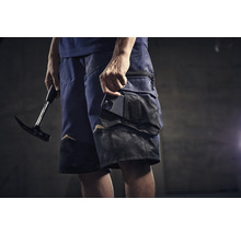 Mann mit Zimmermannskluftshorts, Handy in der Tasche und Hammer in der Hand