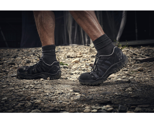 Person mit Arbeitsschuhen auf einem steinigen Untergrund