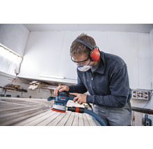 Ein Mann schleift Holz mit einem Exzenterschleifer der Marke Bosch, während er Schutzbrille und Gehörschutz trägt.