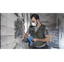 Ein Arbeiter mit Schutzbrille, Maske und Gehörschutz verwendet einen Bohrhammer an einer Wand.