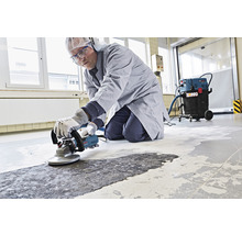 Ein Mann benutzt einen Betonschleifer zur Bodensanierung in Innenräumen.