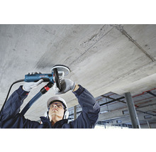 Ein Mann schleift eine Betondecke mit einem Deckenschleifer mit Absaugvorrichtung.