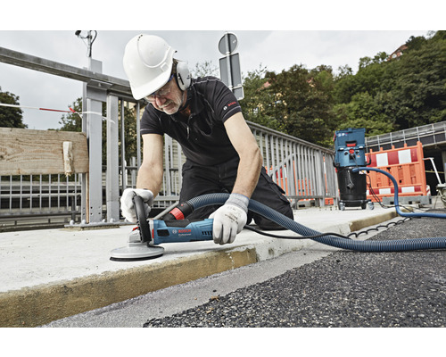 Mann schleift Beton mit einer Betonschleifmaschine von Bosch Professional und einem Staubsauger.